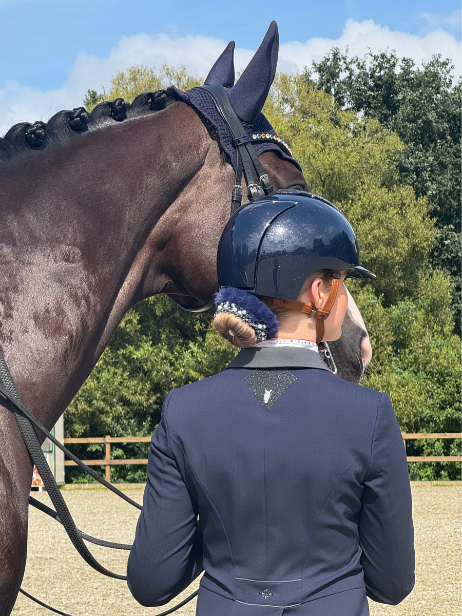 Rider in a navy helmet with a blue BelliNoxx bun, beside a dark horse